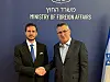 To menn i dress håndhilser foran vegg med tekst Ministry of Foreign Affairs og israelsk flagg.