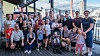 En stor gruppe mennesker står samlet på en terrasse med byutsikt i bakgrunnen.