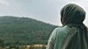 Person med grønt hodetørkle sett bakfra foran et grønt fjellandskap.