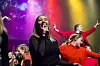 Sanger på scene foran publikum under røde og lilla scenelys.