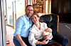 Et smilende par sitter i en lenestol og holder en baby i en lys stue.