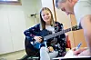 Kvinne spiller gitar i et klasserom mens en mann skriver notater.