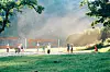 Personer spiller sandvolleyball på utendørs baner i et grønt parkområde.