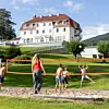 Fire personer spiller strandvolleyball foran en stor hvit bygning med rødt tak.