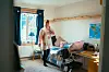 Person står i et soverom med seng, skrivebord, vindu og veggkart.
