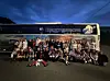 En gruppe fotballspillere poserer foran en lagbuss i kveldsmørket.