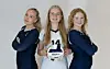 Tre volleyballspillere står side om side og holder en volleyball foran seg.