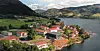 Utsikt over en liten tettbebyggelse ved fjorden med fjell og grønne åser i bakgrunnen.