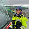 Person i verneutstyr på båt ved oppdrettsanlegg med merder og nett.