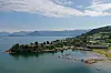 Kystlandskap med øy, småbåthavn og åser i bakgrunnen.