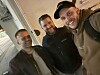 Tre menn smiler i en innendørs selfie, tatt i skrå vinkel.
