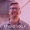 Portrett av en mann med briller og skjegg foran en lys rosa bakgrunn.