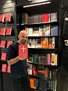 Mann holder en rød bibel foran bokhyller med religiøse bøker.