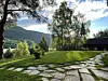 Steinlagt sti gjennom en grønn hage med trær og fjell i bakgrunnen.