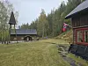 Hytter på en gressplen med skog i bakgrunnen og et norsk flagg ved en rød bygning.