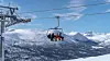 To personer i stolheis over snødekte fjell i solfylt vintervær.
