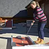 Kvinne spiller minigolf på en takterrasse med en liten bane og ball.