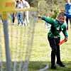 Ung gutt i grønn trøye kaster frisbee på en gressplen med personer i bakgrunnen.