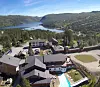 Hotellbygninger med basseng, omgitt av skog og fjell ved en innsjø.
