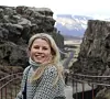 Smilende kvinne foran en kløft med fjell og snø i bakgrunnen.