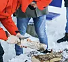 Person i rød jakke sager en vedkubbe i snøen utendørs.