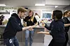 To ansatte i et kontorlandskap snakker og bruker håndbevegelser mens andre står i bakgrunnen.