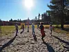 Barn spiller volleyball på en sandbane under sterk sol, med trær i bakgrunnen.