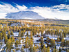 Snødekt fjell over en skogkledd dal med høstfarger og noen små hytter.