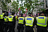 Politifolk i gule vester står i linje foran demonstranter med flagg i en gate i London.