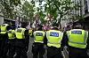 Politifolk i gule vester står i linje foran demonstranter med flagg i en gate i London.