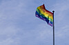 Et pride-flagg vaiers på en høy flaggstang mot blå himmel.