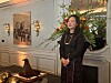 Kvinne står ved en stor blomsterdekorasjon i et elegant rom med speil og veggkunst.