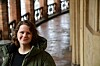 Maria Selbekk står i en historisk innendørs gang med buede vinduer og steinvegger.