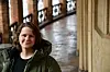 Maria Selbekk står i en historisk innendørs gang med buede vinduer og steinvegger.