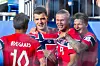 Fire fotballspillere i røde drakter jubler tett sammen på fotballbanen.