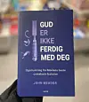 Hånd holder en blå bok med tittelen «GUD ER IKKE FERDIG MED DEG» foran en uskarp bakgrunn.