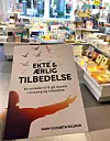 Bok med tittelen «Ekte & ærlig tilbedelse» holdes opp i en bokhandel med bøker rundt.