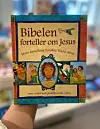 Hånd holder en bok med tittelen «Bibelen forteller om Jesus».