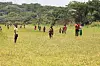 Flere barn på en åpen gresslette med skog og åser i bakgrunnen.