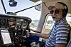 Pilot i cockpit med instrumentpanel, headset og solbriller.