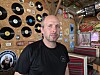 Mann foran vegg med vinylplater og musikalsk dekor i et rustikt barrom.