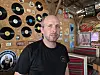 Mann foran vegg med vinylplater og musikalsk dekor i et rustikt barrom.