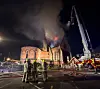 Brannvesen slukker en bygning i brann om natten, med røyk, flammer og stigebil.