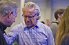 Bill Johnson i blå skjorte samtaler med en mann i et konferanselokale.
