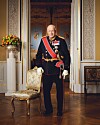 Uniformert person med medaljer står i en rikt dekorert sal.