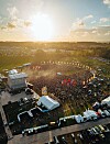 Luftfoto av en musikkfestival med scene, publikum og telt i kveldssol.