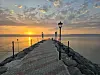 Brosteinslagt molo med lyktestolpe og solnedgang over stille sjø.