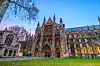 Westminster Abbey i London med utsmykket fasade, grønne plener og blå kveldshimmel.