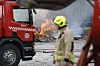 Brannmann foran rød brannbil med flammer og røyk i bakgrunnen.