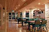 Restaurantinteriør med grønne stoler, bord, trepanel i taket og steinvegger.